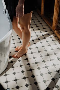 Home A young woman stands barefoot on sunlit tiled bathroom floor, emphasizing relaxation.
